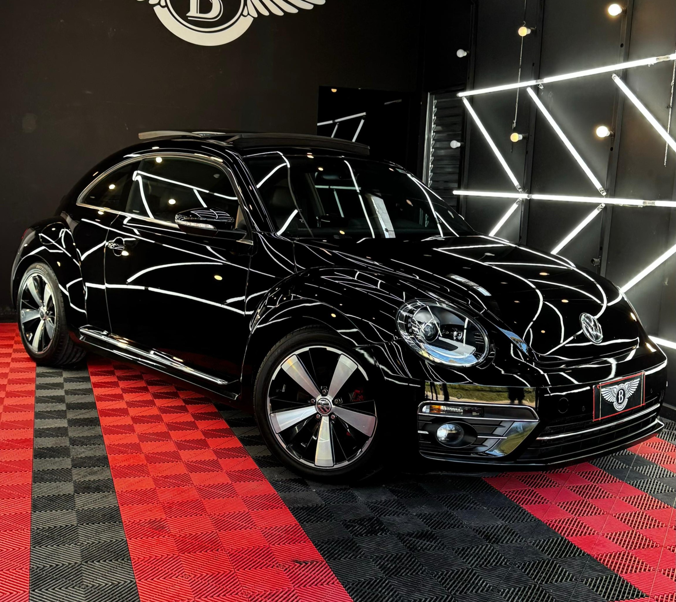 A black car in a showroom with a checkered floor and illuminated wall panels